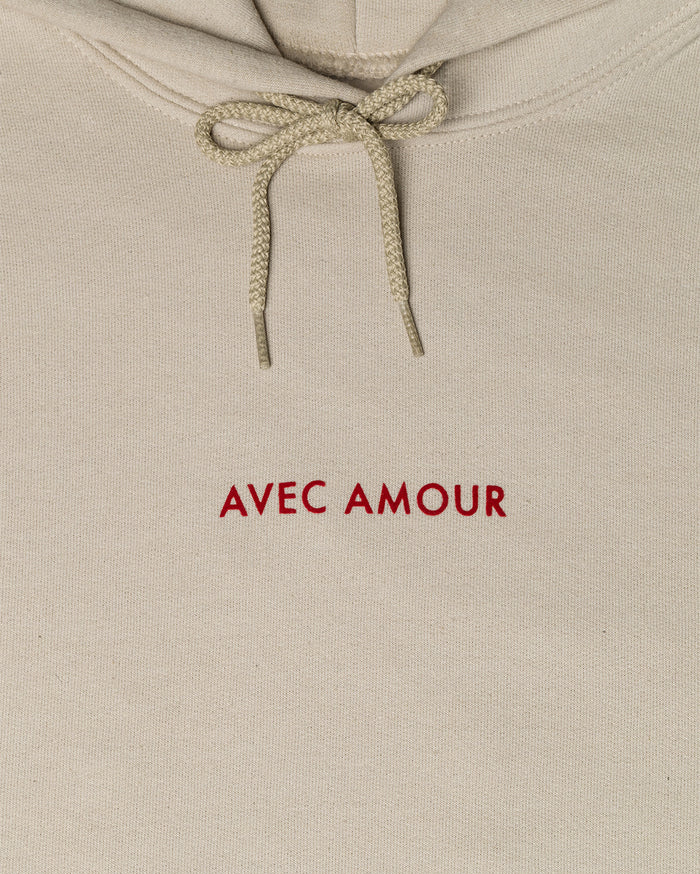 Beige hoodie with drawstrings and red embroidered text 'AVEC AMOUR'.