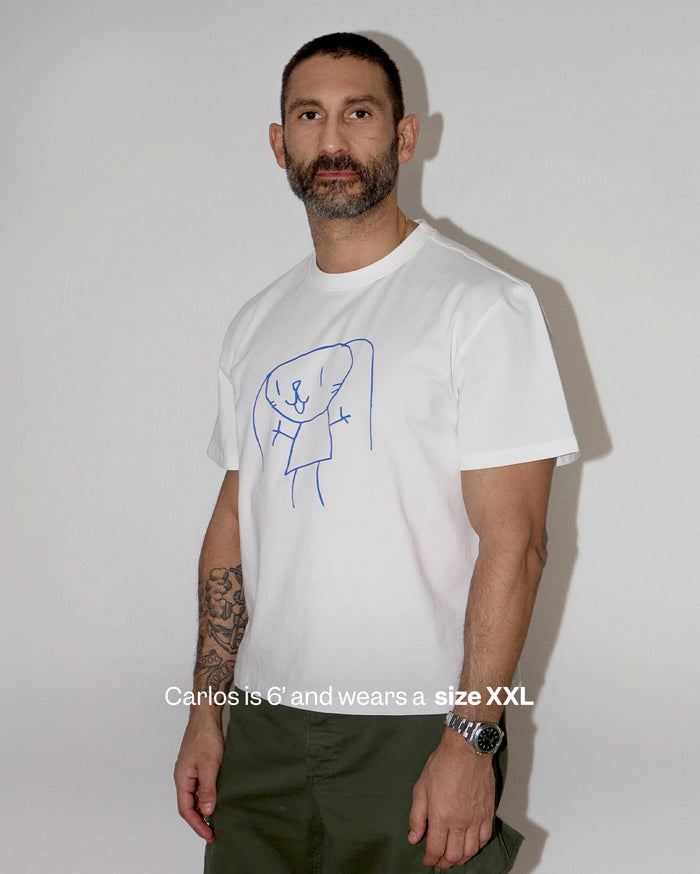 Carlos is 6' and wears a size XXL. He has medium skin tone and wears a white t-shirt with a blue cartoon character drawing, olive green pants, and a silver watch.