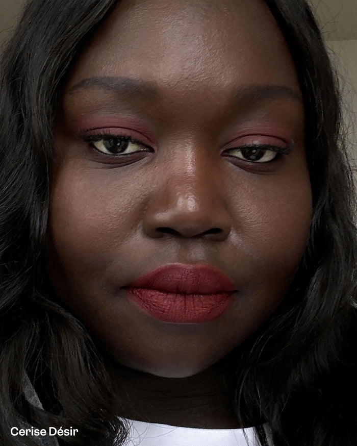 Cerise Désir. Close-up of a model with deep skin tone wearing matte deep red lipstick and matching reddish eyeshadow.