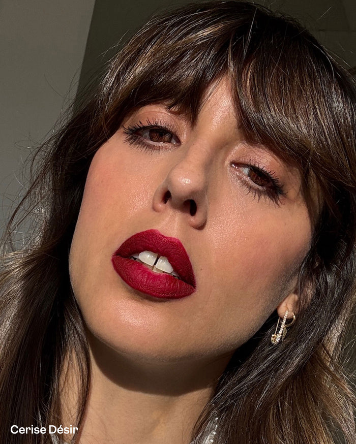 Cerise Désir. Close-up of a woman with medium skin tone wearing deep red lipstick, her mouth slightly open, revealing teeth.