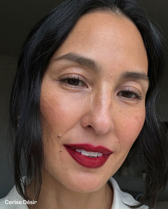 Woman with medium skin tone wearing Cerise Désir, a vibrant deep red lipstick.