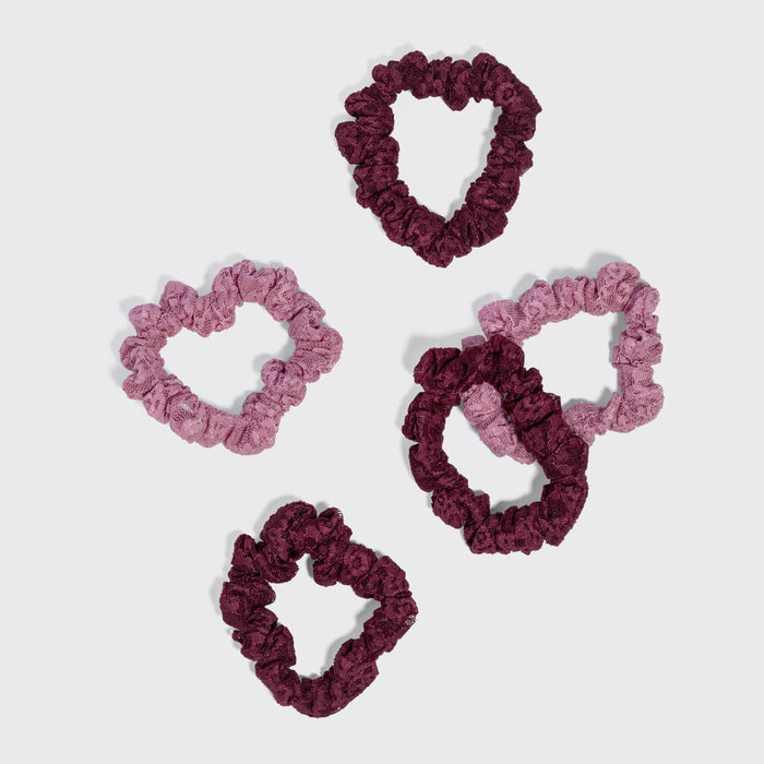 Five ruffled scrunchies in two shades of pink and two shades of deep burgundy, arranged on a light gray background.