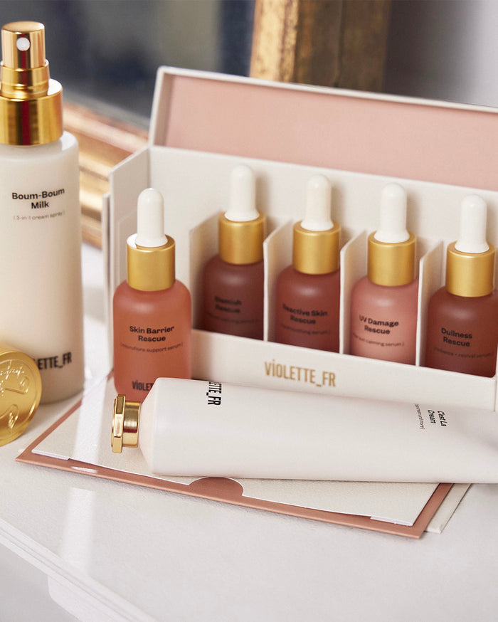 Violette_FR skincare products including Boum-Boum Milk (3-in-1 cream spray), C'est La Cream (hydrates and more), and a set of five serums: Skin Barrier Rescue, Blemish Rescue, Reactive Skin Rescue, UV Damage Rescue, and Dullness Rescue, displayed on a white surface.