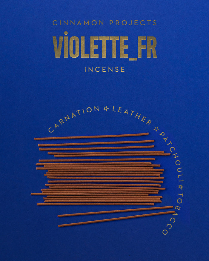 CINNAMON PROJECTS VIOLETTE_FR INCENSE. Brown incense sticks are piled on a deep blue background, with the words CARNATION ☆ LEATHER ☆ PATCHOULI ☆ TOBACCO curved around them.