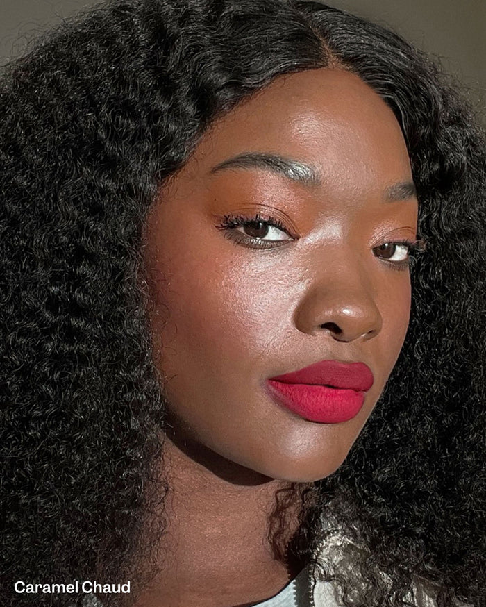 A woman with deep skin tone and dark curly hair wears vibrant red lipstick. The text "Caramel Chaud" is visible.