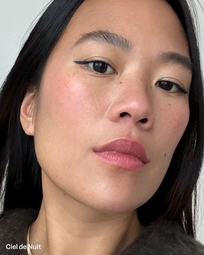 Ciel de Nuit. Close-up of a woman with medium skin tone wearing rosy-mauve lipstick, soft pink blush, and black winged eyeliner.