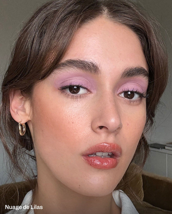 Nuage de Lilas. Close-up of a model with medium skin tone wearing light purple eyeshadow and glossy peachy-pink lips.