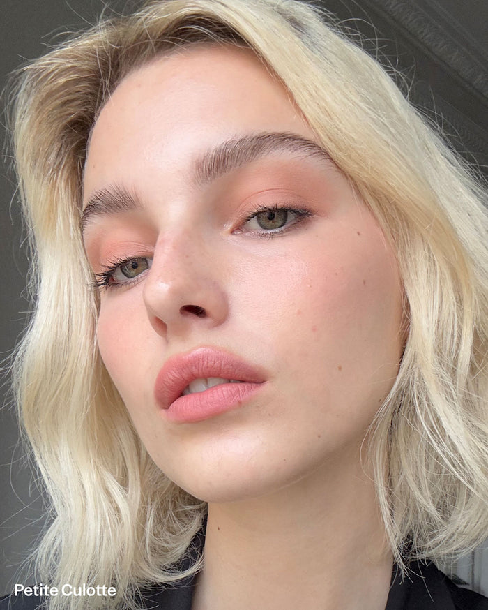 Petite Culotte. Close-up of a light-skinned model with blonde hair and green eyes, wearing peachy-pink eyeshadow and matching lipstick.