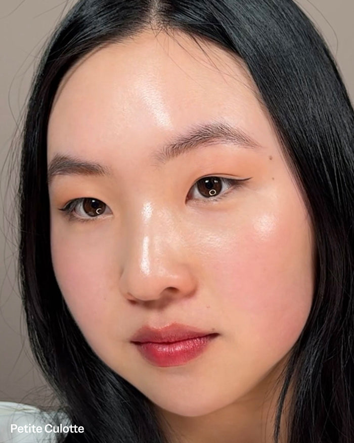 Petite Culotte. Close-up of a model with light skin tone, dark hair, wearing subtle eyeliner, dewy complexion, and glossy reddish-pink lips.
