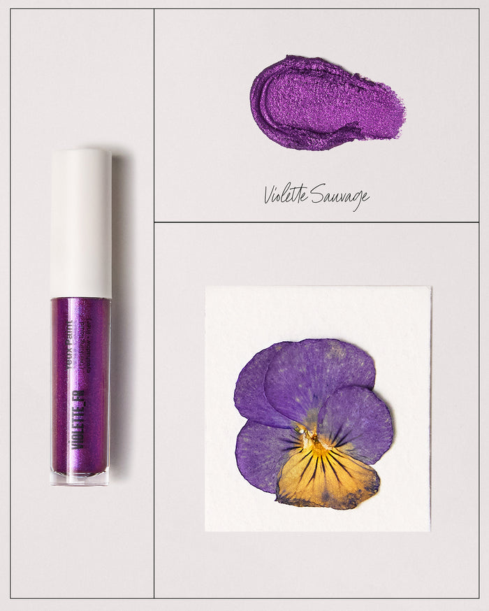 Violette_FR Yeux Paint twinkling liquid eyeshadow "" in Violette Sauvage. The image shows the clear tube, a shimmery purple swatch, and a pressed purple and yellow pansy flower.