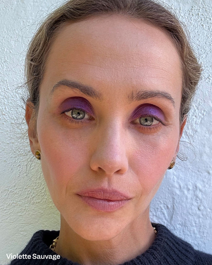 Violette Sauvage. Close-up of a woman with light skin tone wearing vibrant purple eyeshadow and natural pinkish-mauve lipstick.